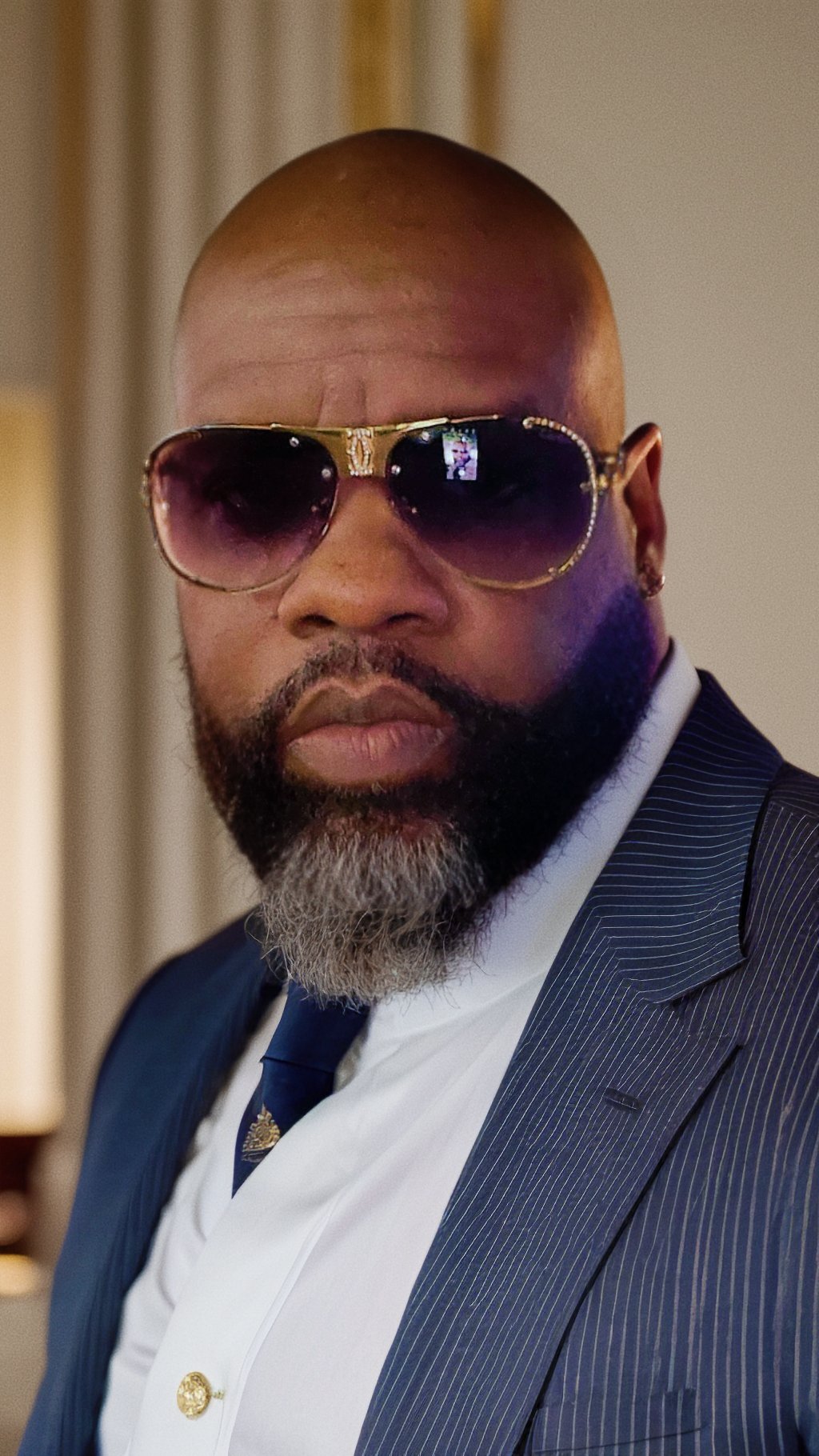 Portrait of Ditonion Brown, co-founder of DiLa Enterprises LLC, wearing a navy pinstripe suit with a blue tie and dark sunglasses, photographed outdoors against a bright sky.